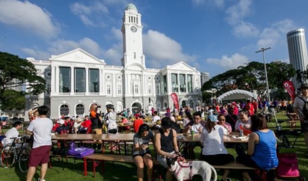 A crowd of people eat at picnic tables on a lawn in front of Victoria Theatre in Singapore.