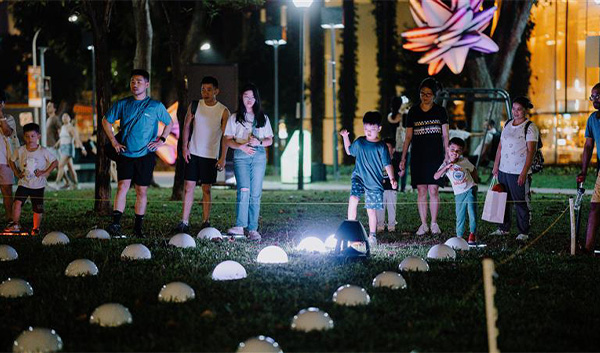 People at night at a park with glowing dome-shaped lights in the grass.