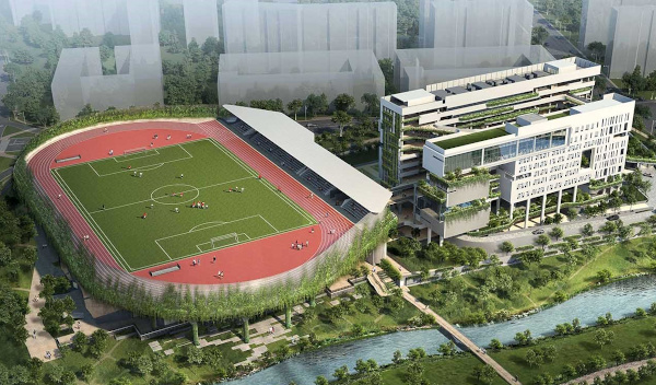 Aerial view of a modern school building with a track and field stadium next to a river.
