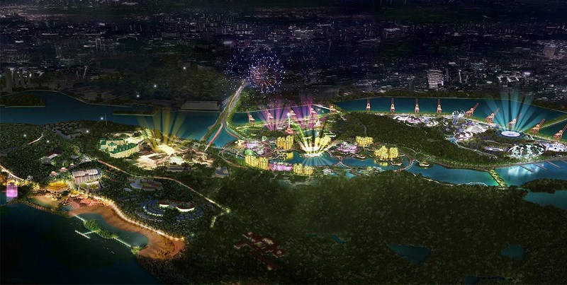 Aerial view of a lit-up cityscape with a theme park, fireworks, and water features at night.