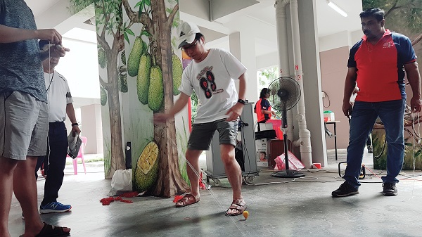 A man demonstrates how to spin a top in an indoor space with observers and painted pillars.