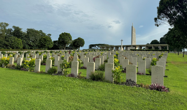 Rows of headstones in a war cemetery, with a memorial building in the background.