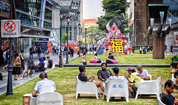 City park with people sitting on lawn chairs, festive decor, and a "no skating" sign.