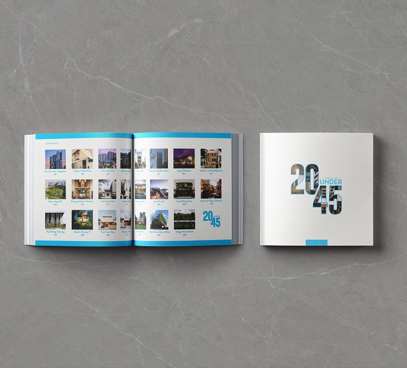 Open book titled "20 Under 45" with building photos, next to a closed book of the same title on a gray surface.