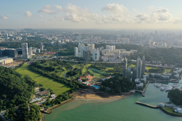 Aerial view of Singapore's coastline with buildings, greenery, and a marina.