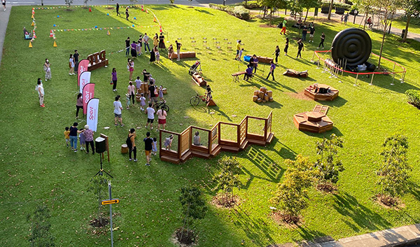 Outdoor event on grass with people near obstacle course, branded flags, and large inflatable.