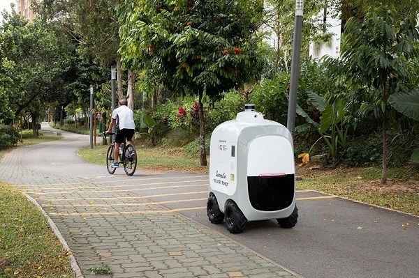 A Camello delivery robot on a path, with a cyclist in the background.