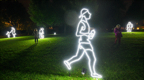 Neon light outlines of running figures on a dark grassy park at night