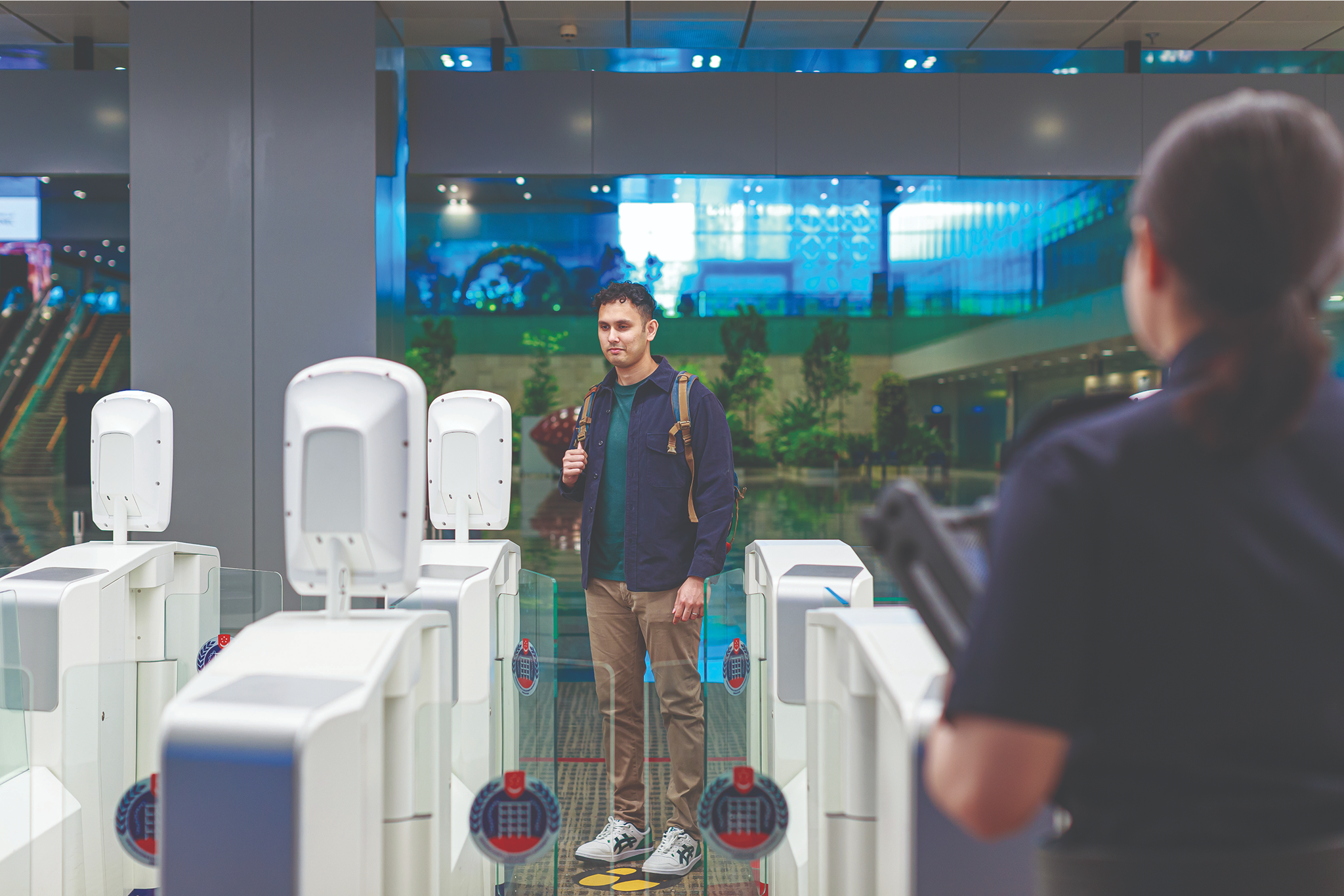 A man walks through an automated security gate as an agent watches.