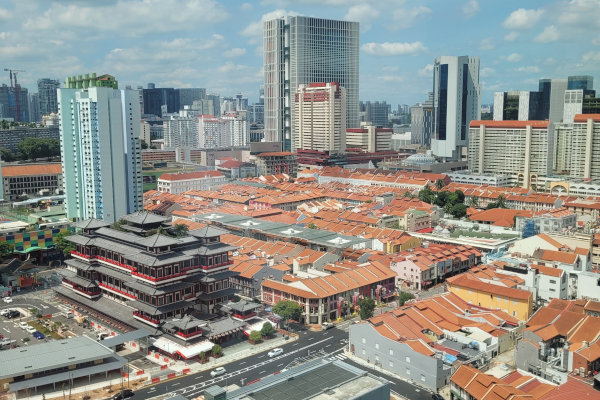 Singapore cityscape: Buddhist temple, orange rooftops, and skyscrapers under a partly cloudy sky.