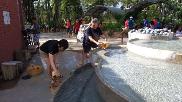 People enjoying a foot bath at Beitou Thermal Valley, Taiwan. They are scooping water with wooden buckets.
