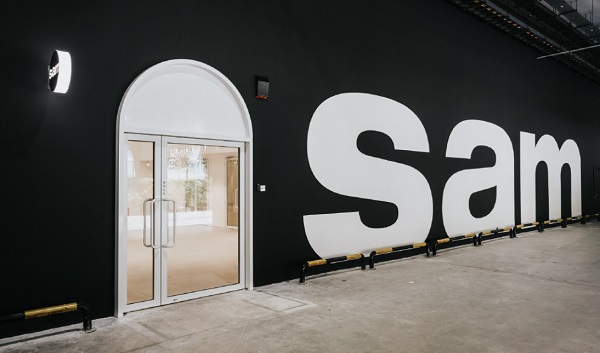 Building exterior with black wall, "Sam" in large white letters, and a white arched doorway.