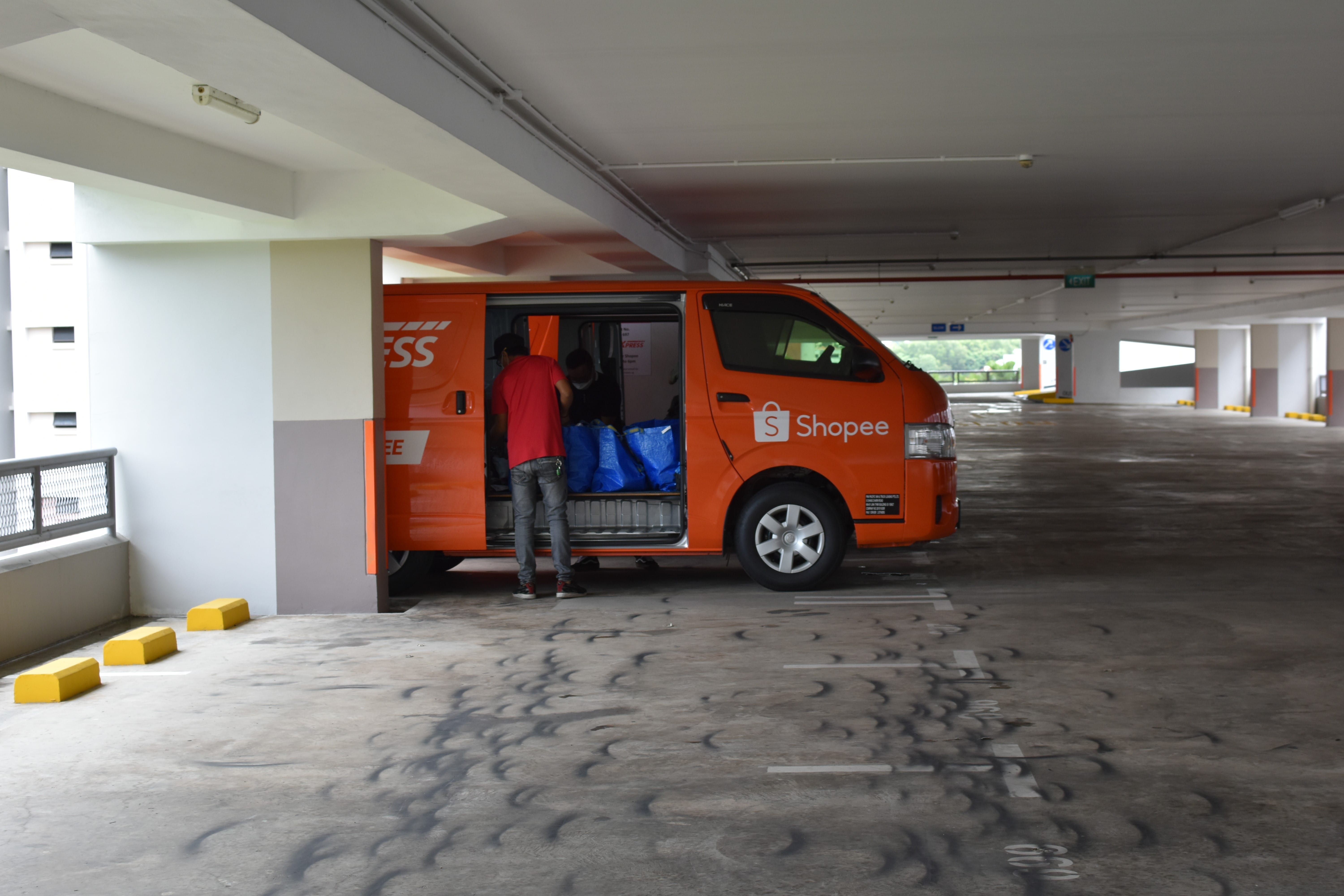 Delivery worker loading parcels into a Shopee van in a multi-storey car park.