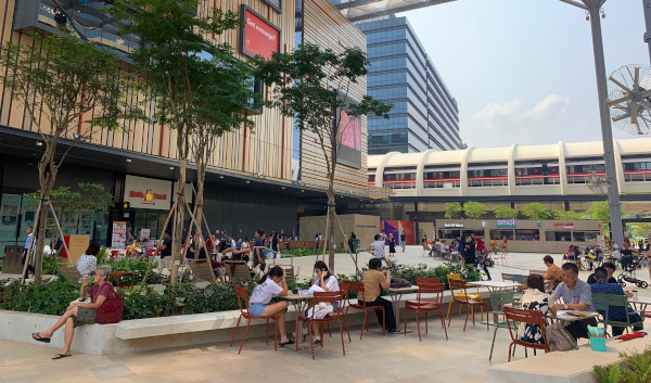 Outdoor scene with people seated at tables near shops and a train line on a sunny day.