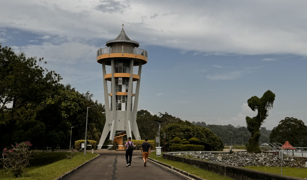 Two people walk towards an observation tower in a park on a cloudy day.
