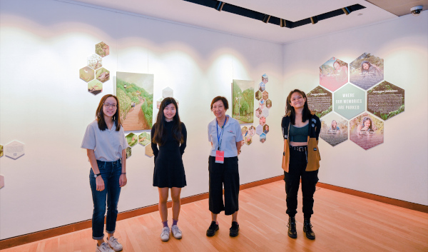 Four women stand in an art gallery with artwork featuring nature scenes and text.