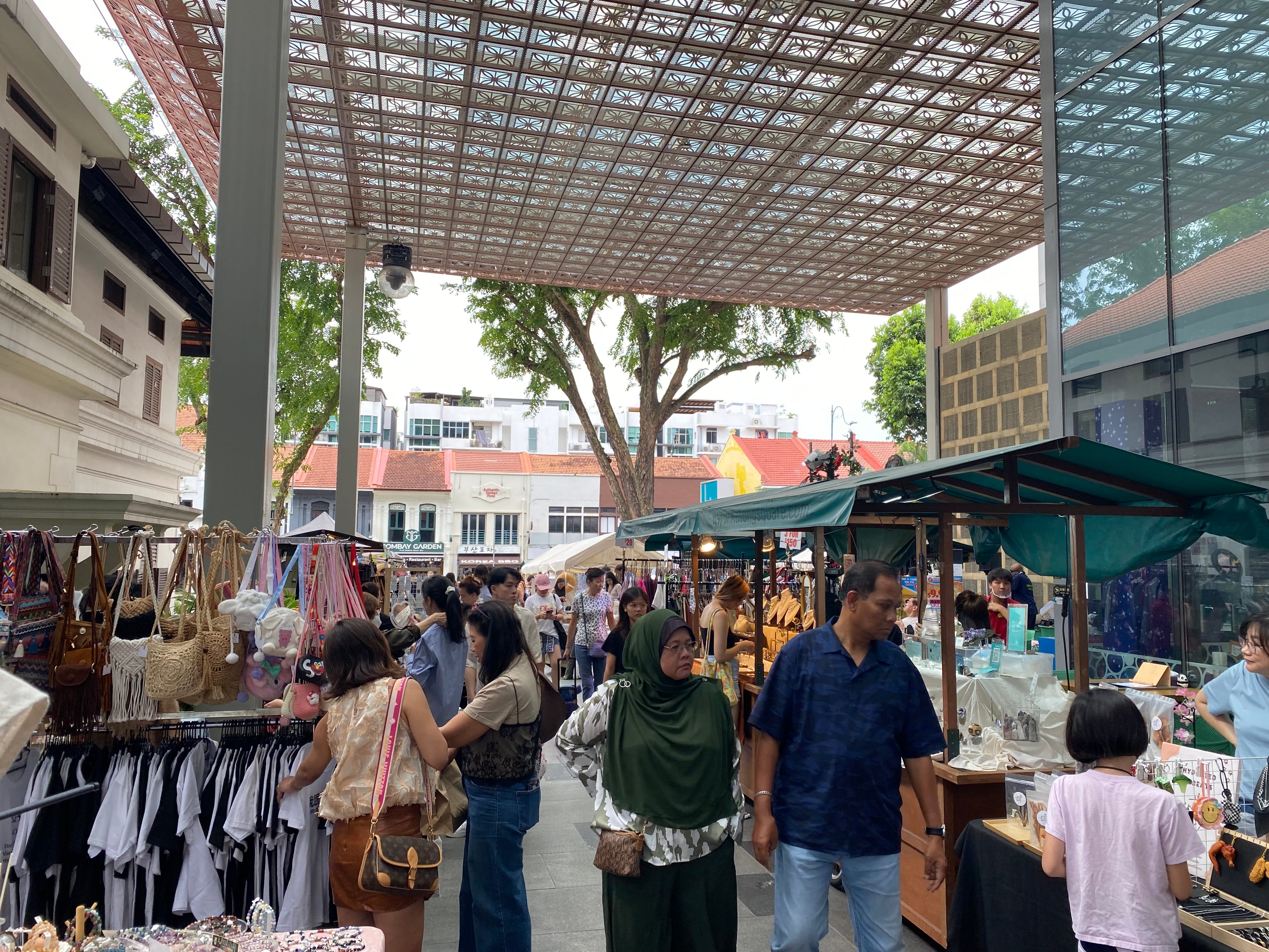 Outdoor market in Singapore with people browsing vendor stalls under a decorative canopy.