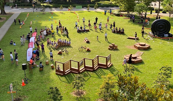 Outdoor community event on grass with people, obstacles, and activity stations.