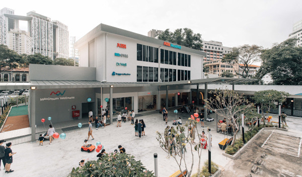 Exterior view of Maximum Wellness center with people and balloons in a plaza.
