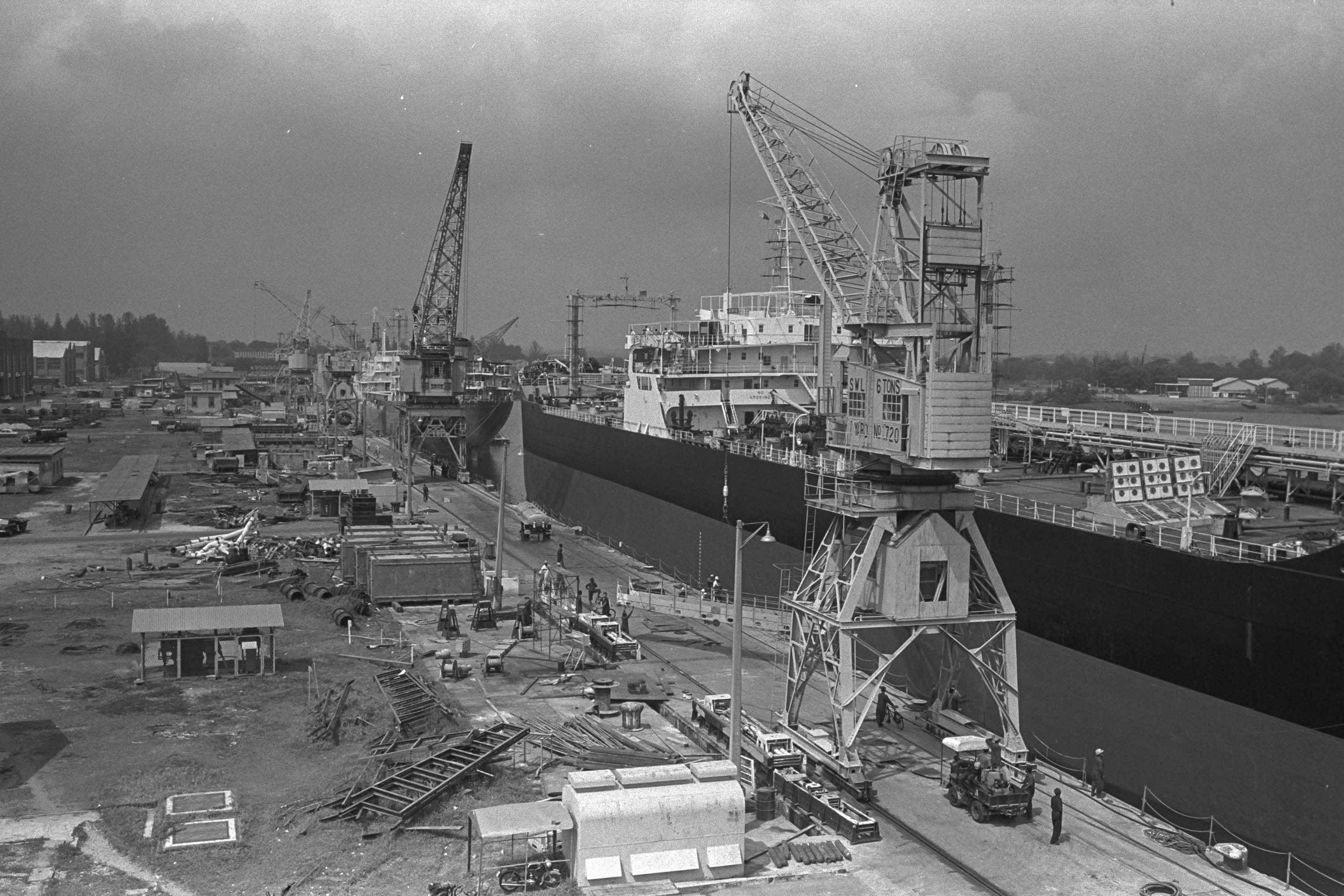 Black and white photo of a shipyard with cranes and a large ship.