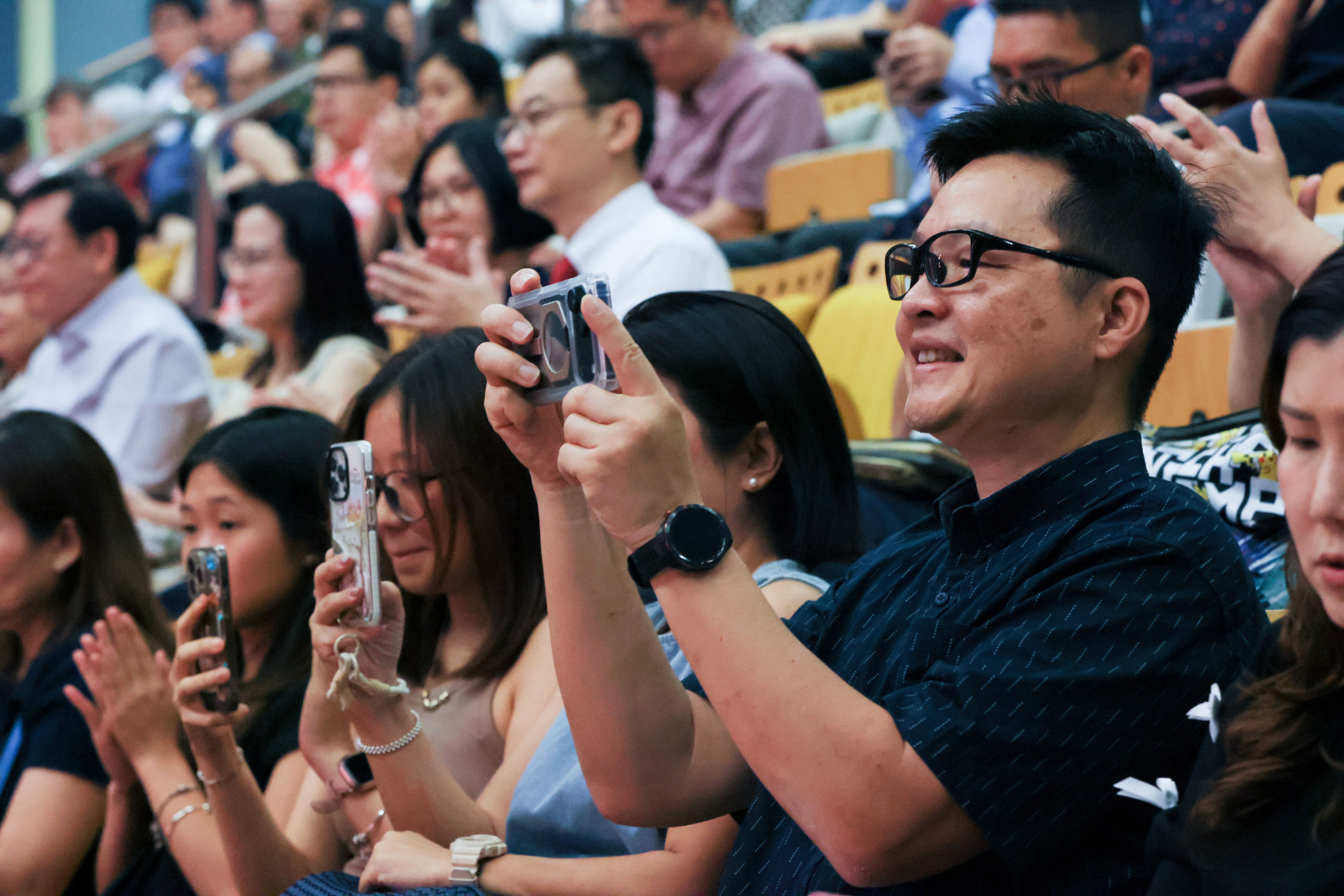 Image of the audience smiling and taking photos at the TP Scholarships Presentation