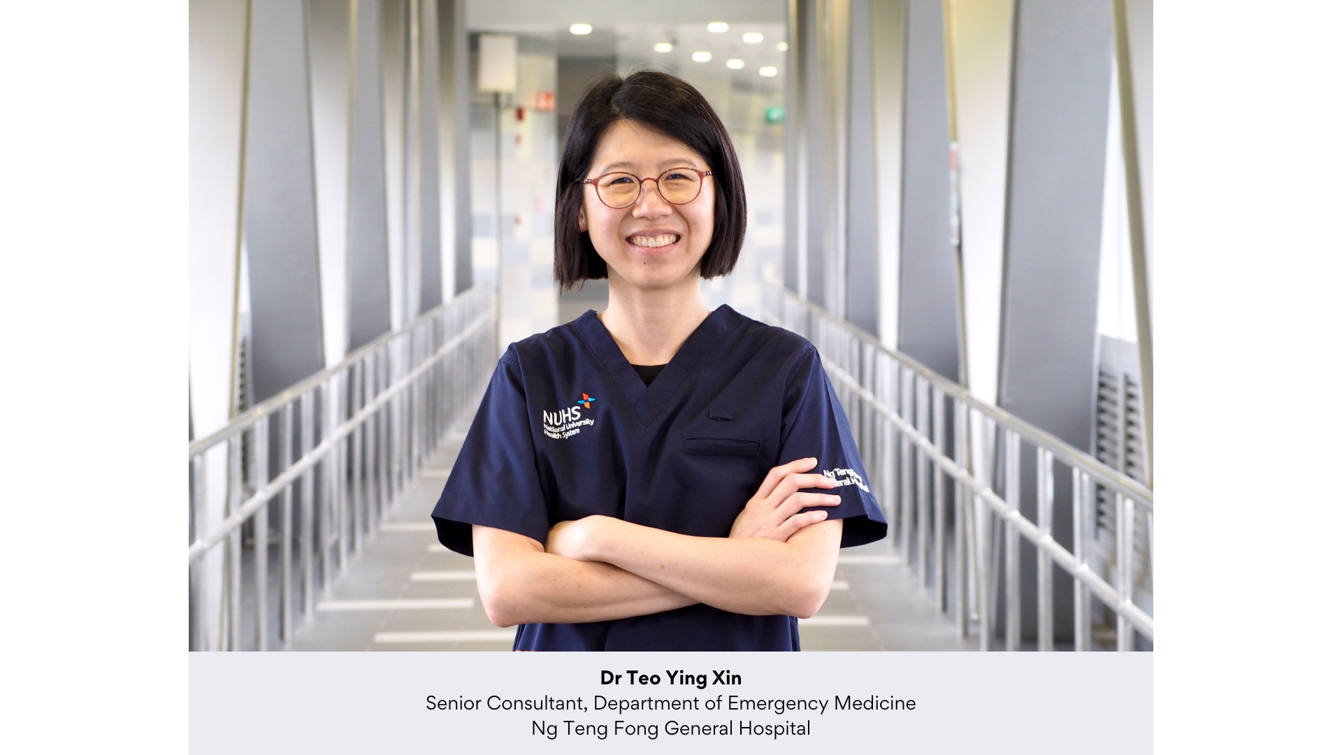 Dr Teo Ying Xin, smiling woman in navy NUHS scrubs with arms crossed, standing in a hospital corridor.