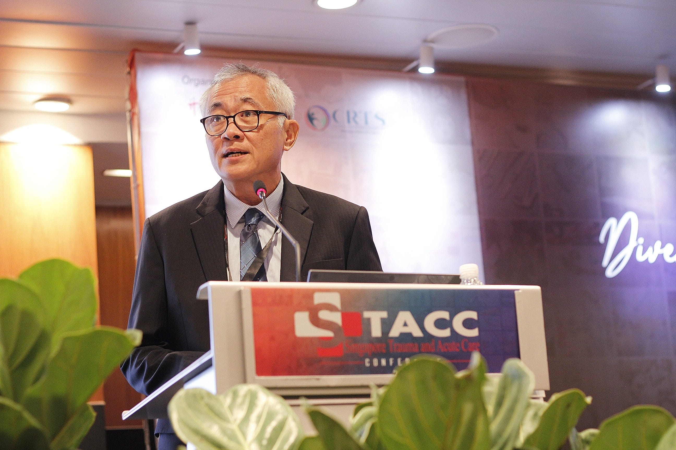 A man with glasses and gray hair speaks at a podium labeled STACC Singapore Trauma and Acute Care Conference.