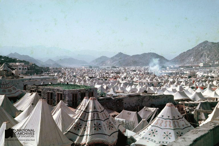 A vast field of white decorated tents stretches toward rocky mountains under a pale blue sky.