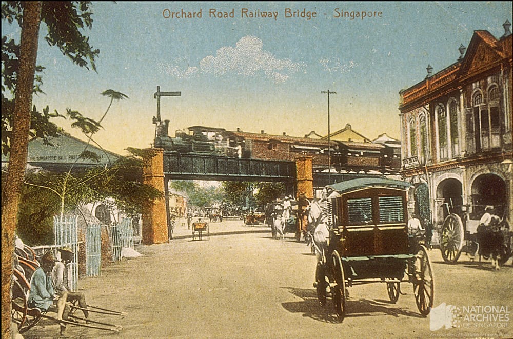 Vintage postcard of Orchard Road Railway Bridge in Singapore with a steam train, horse carriages, and colonial buildings.