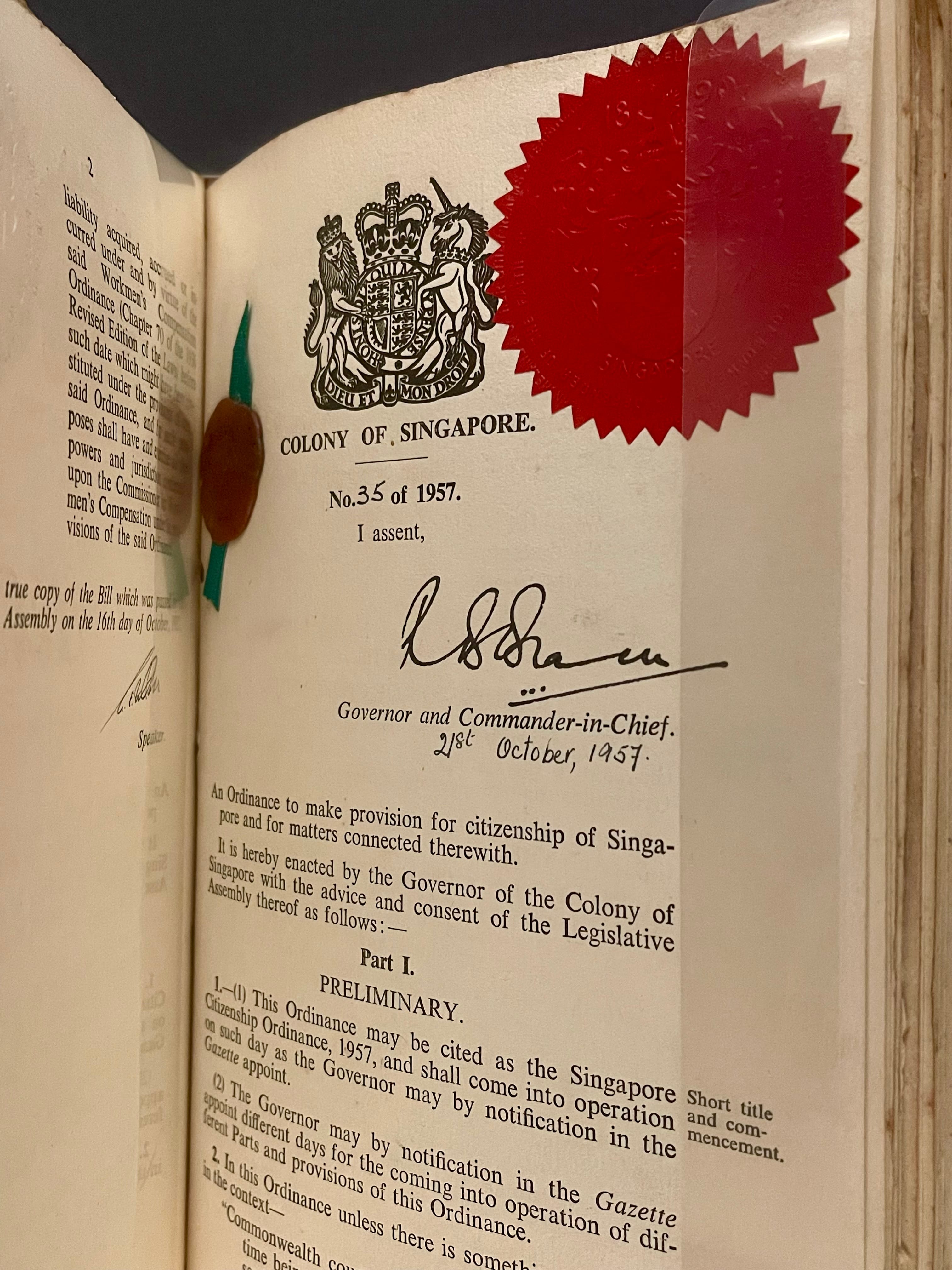 An open book showing a Colony of Singapore ordinance No. 35 of 1957, signed by the Governor, with a red wax seal.