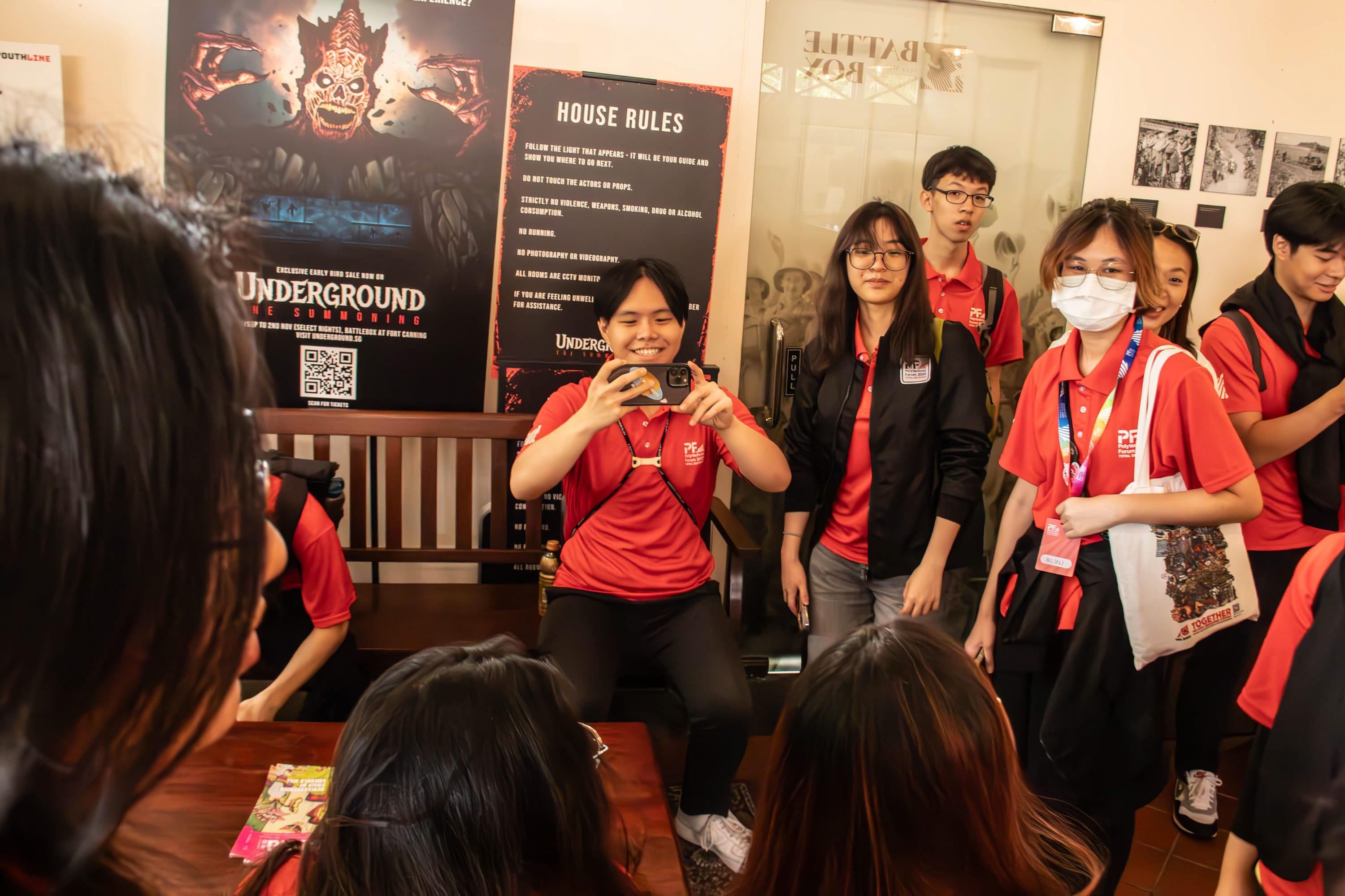 Group of young people in red polo shirts inside a venue with a House Rules sign and Underground event poster.