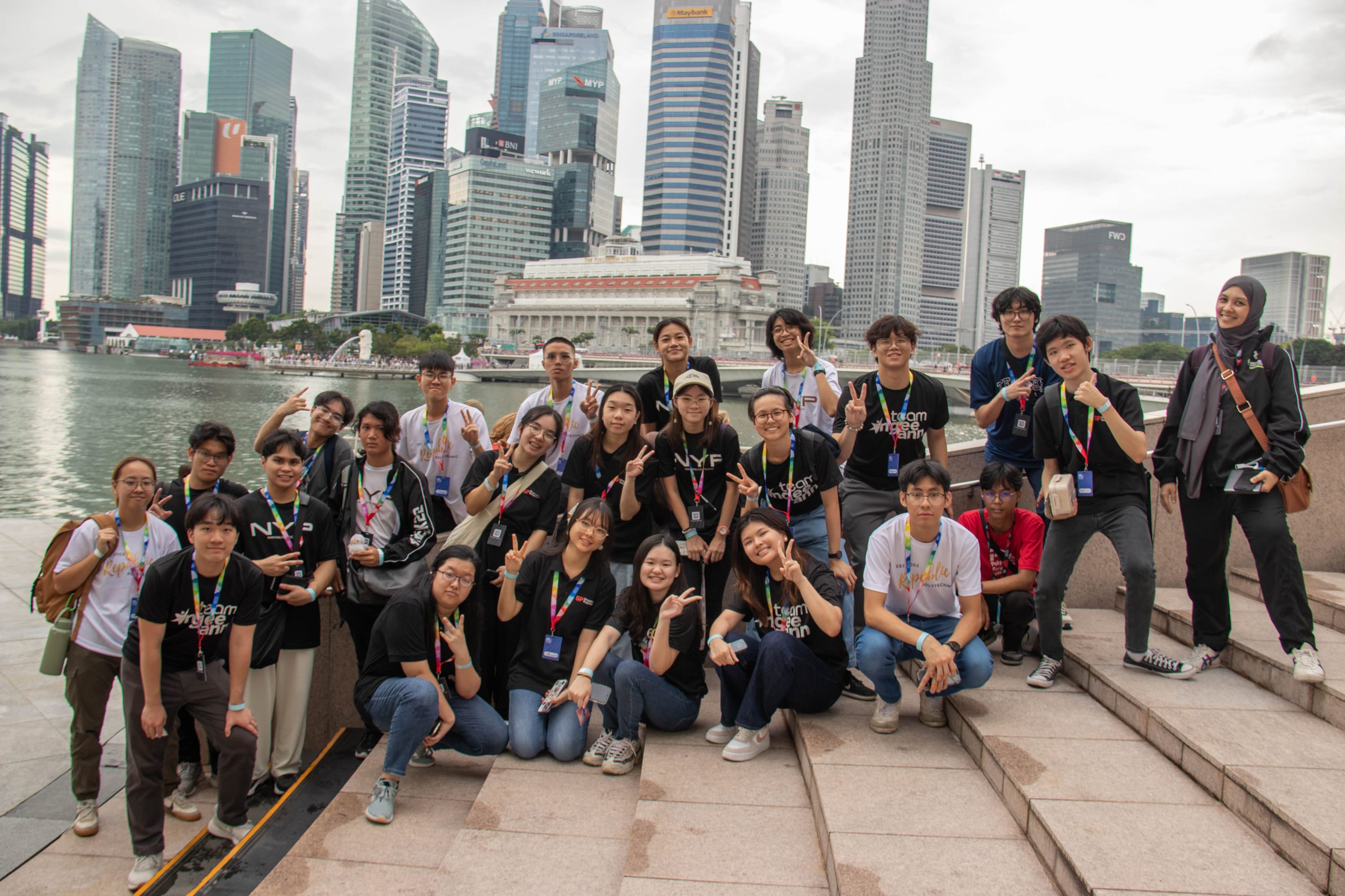 A large group of young people posing with peace signs on steps near Singapore's Marina Bay skyline.