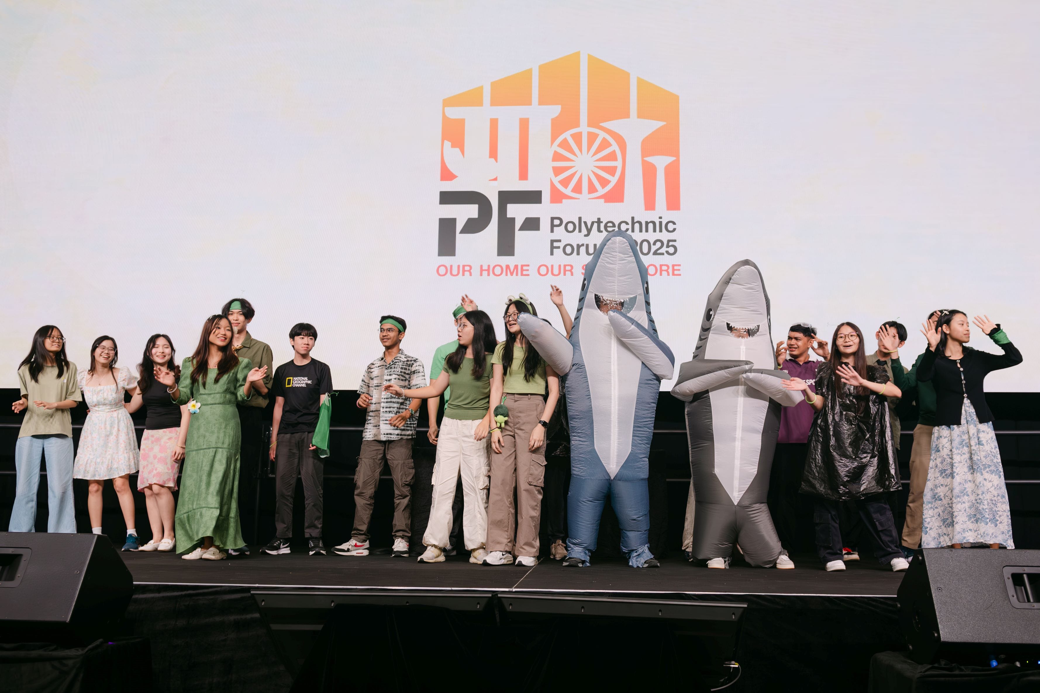 A group of young people on stage at Polytechnic Forum 2025, two wearing inflatable shark costumes.