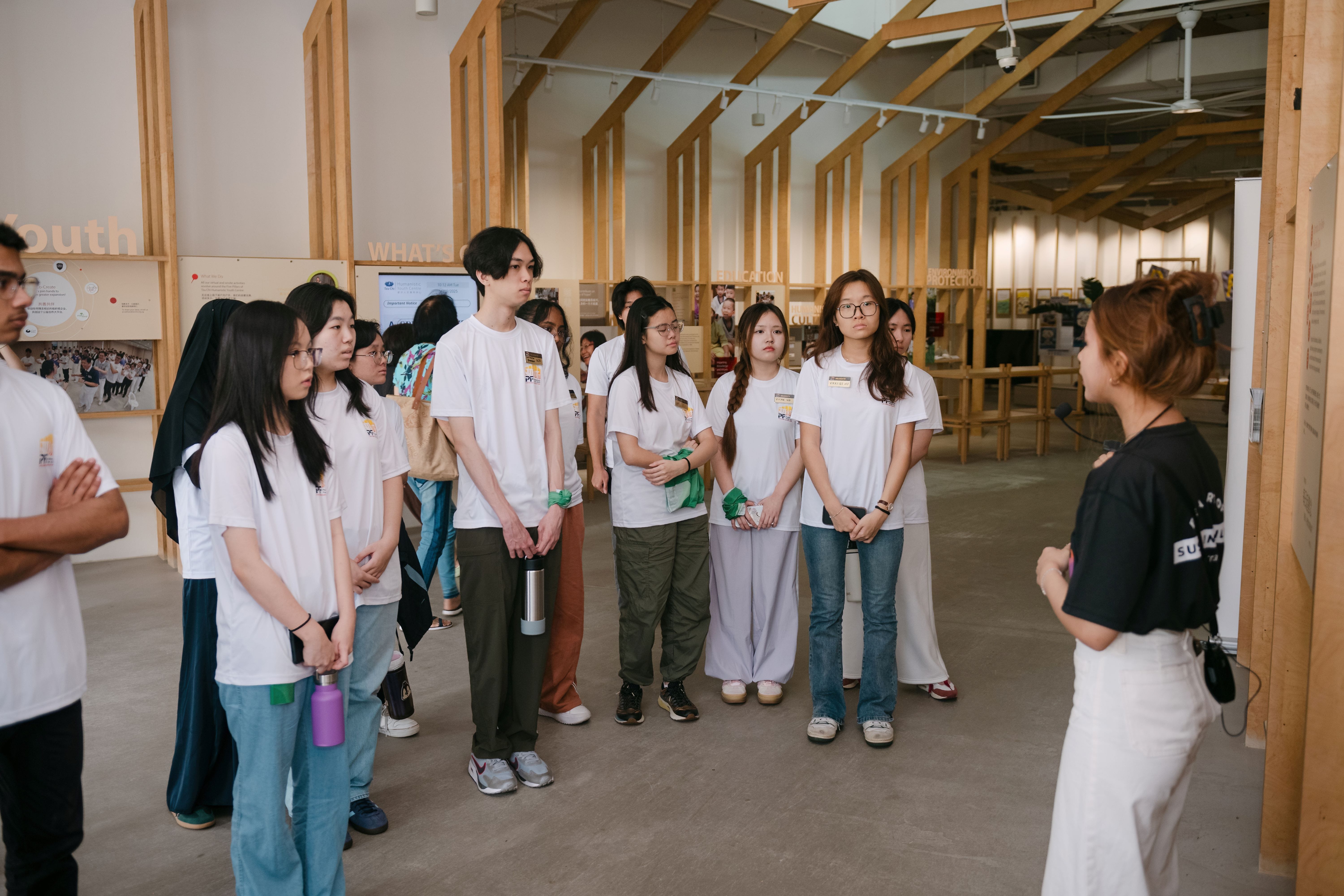 A group of young people in white shirts listens to a guide inside a museum with wooden frame displays.