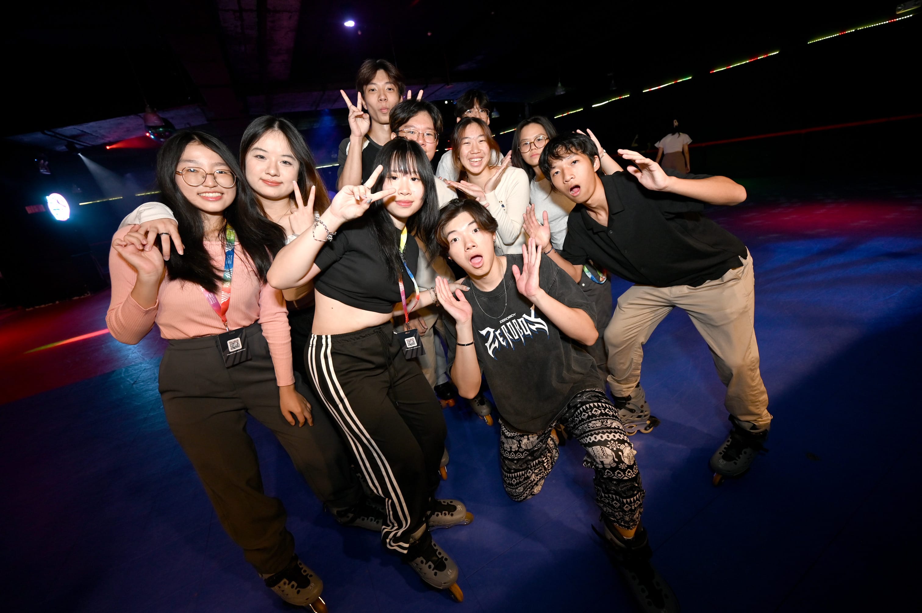 A group of young people on roller skates pose and make fun gestures at a dimly lit skating rink with colorful lights.