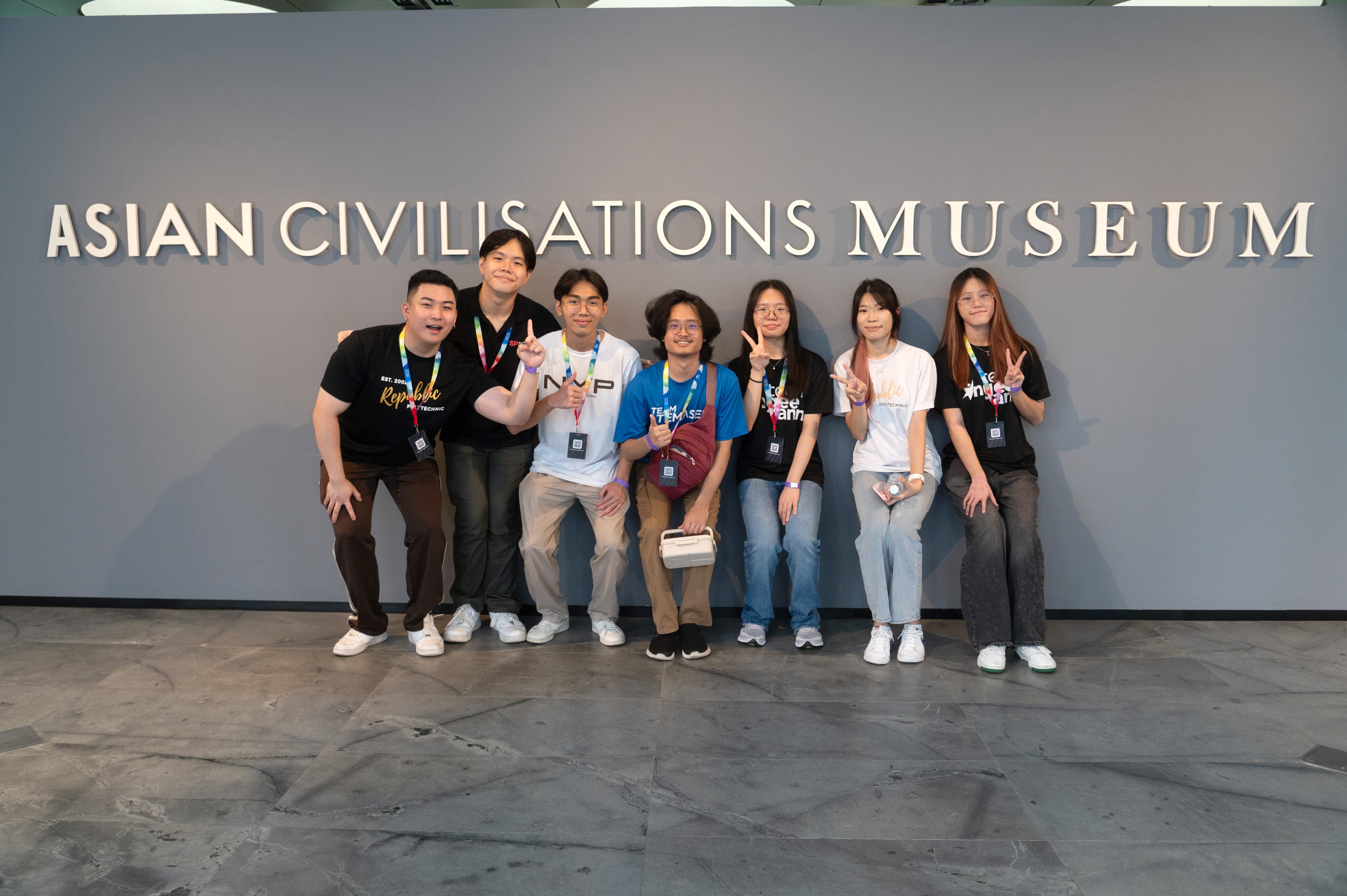 Seven young people pose and smile in front of the Asian Civilisations Museum sign, some making peace signs.