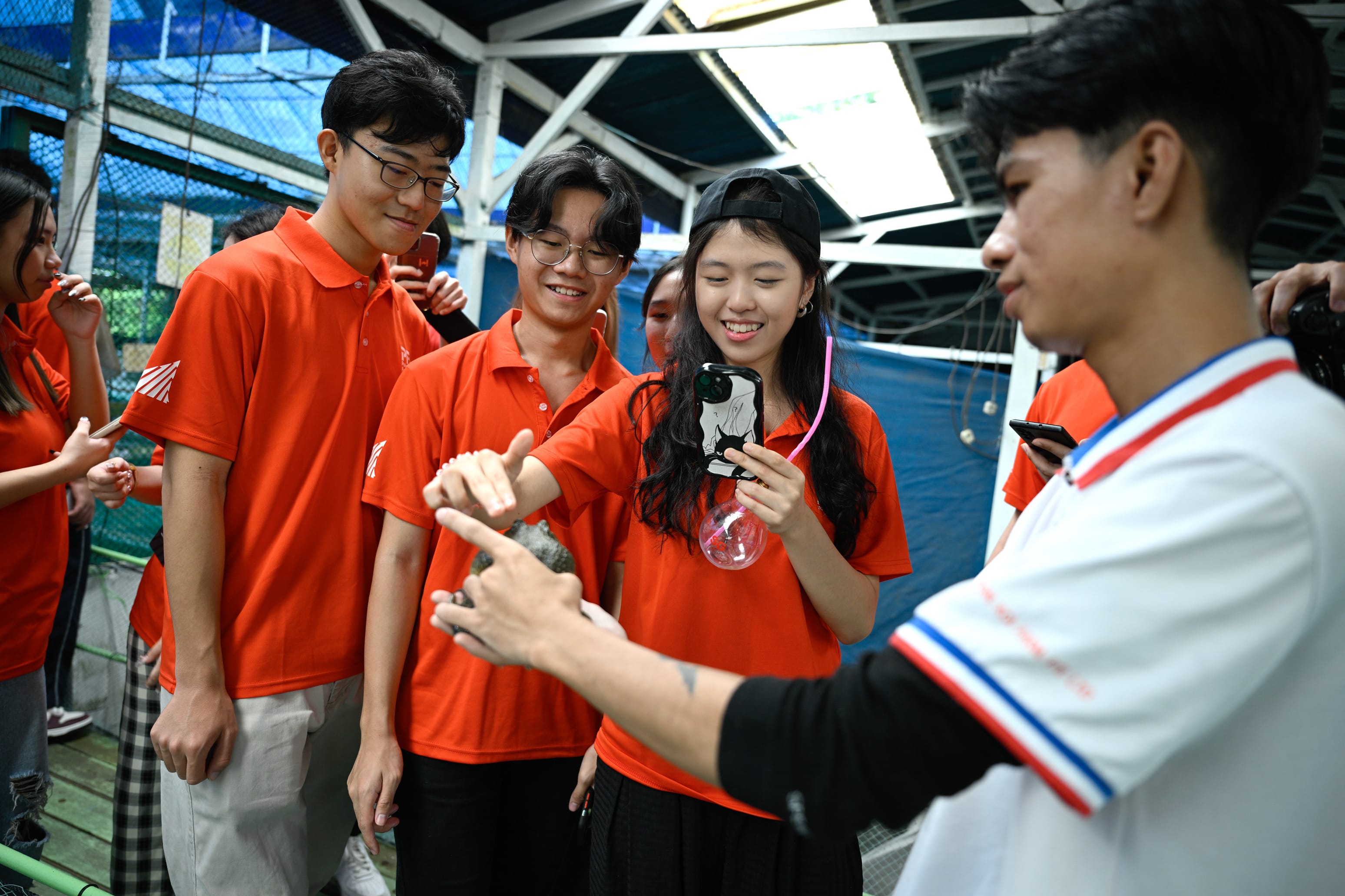 A group of young people in orange shirts gather smiling around a person holding a small animal indoors.