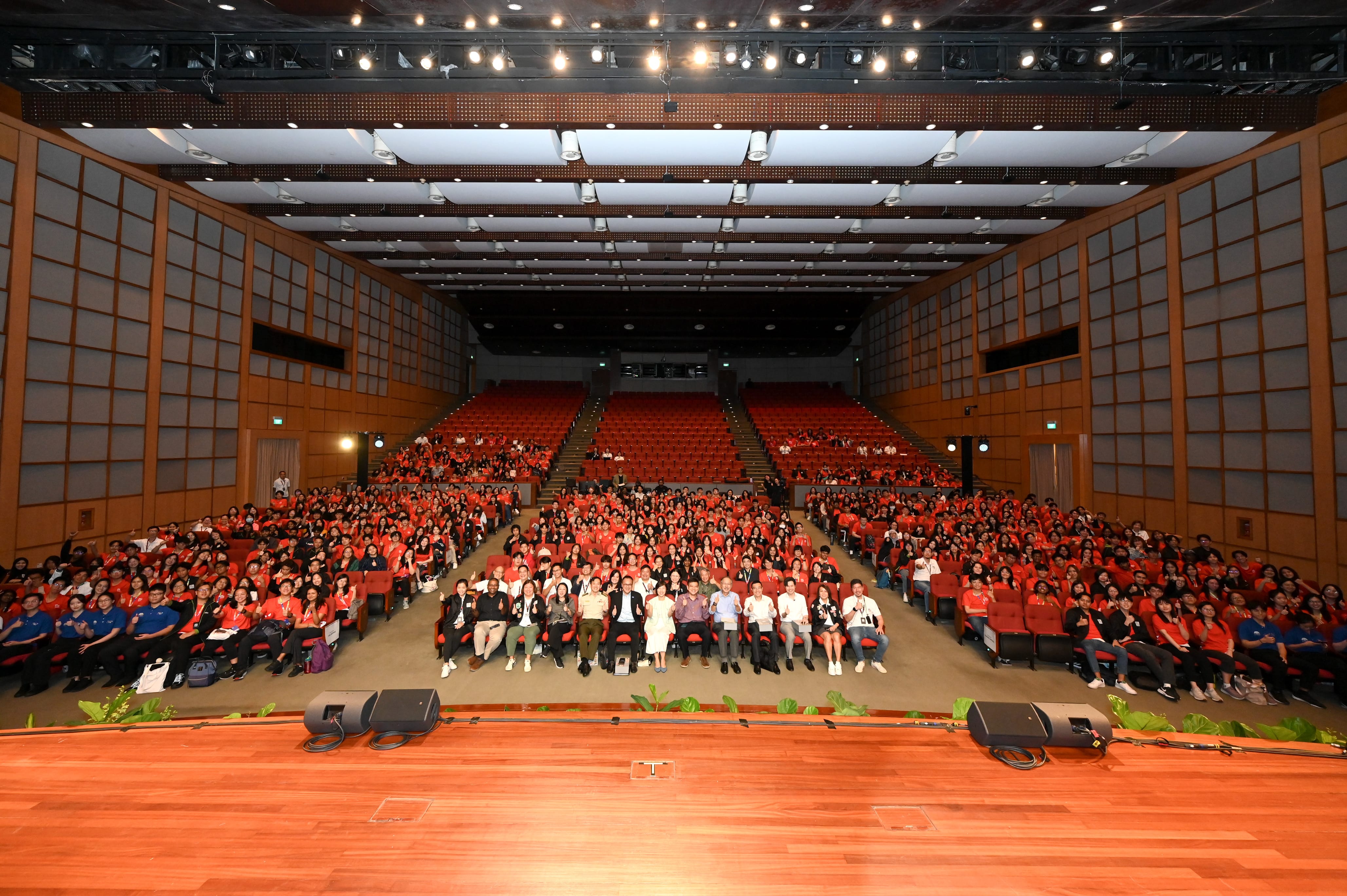 A large auditorium filled with hundreds of attendees mostly wearing red shirts, viewed from the stage.