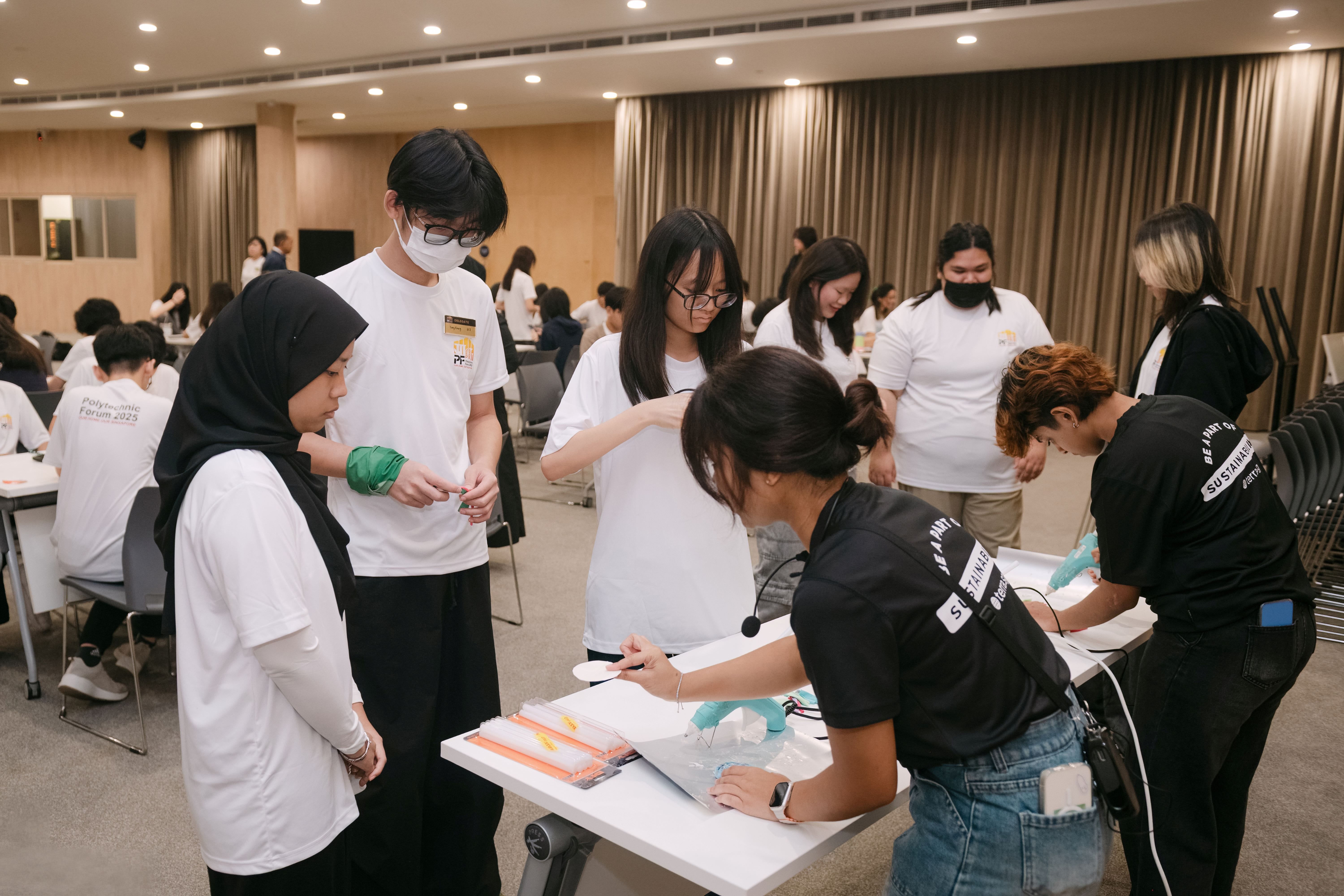 Students in white shirts gather around a table at Polytechnic Forum 2025, watching a facilitator in black write on materials.