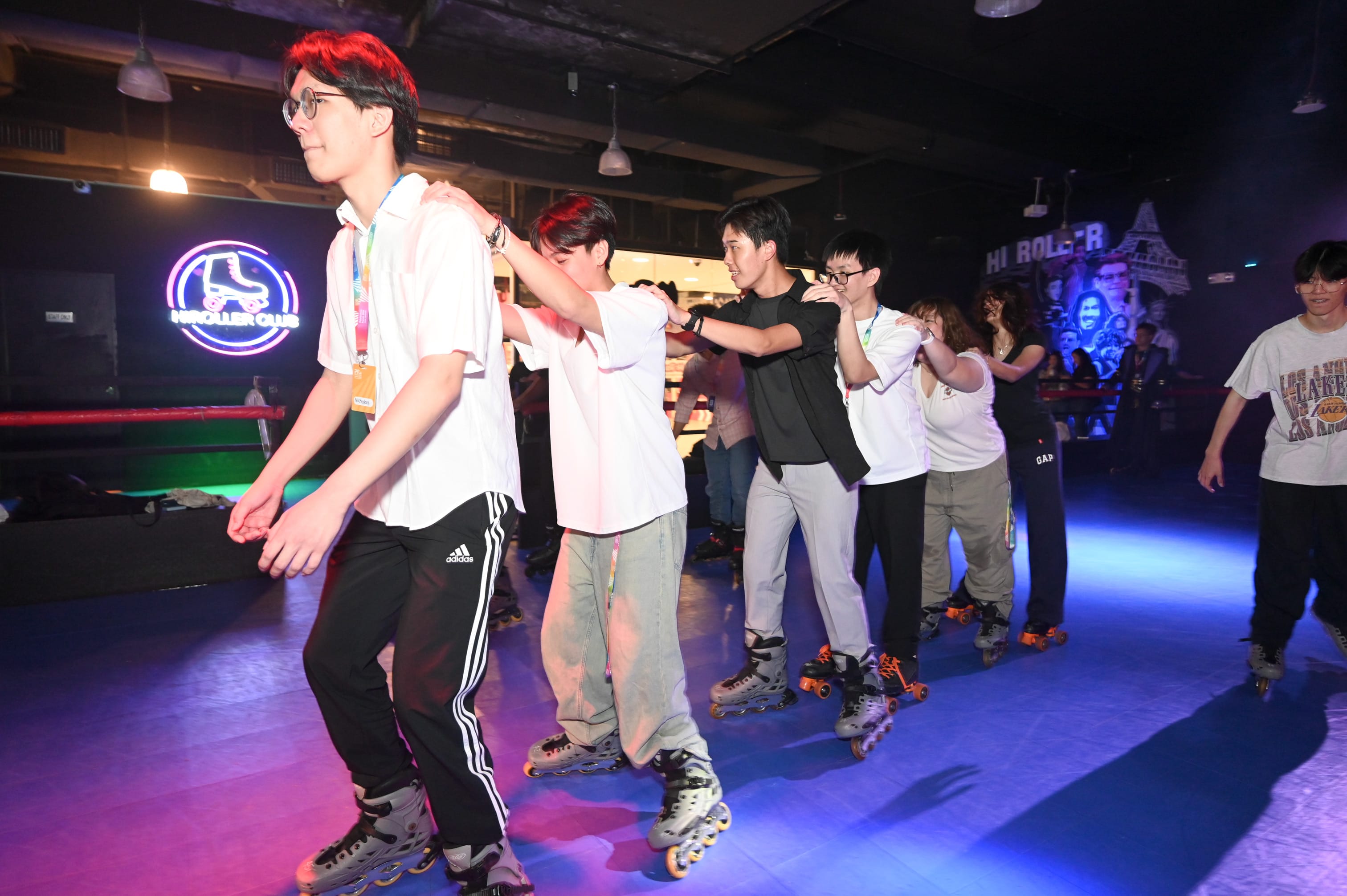 A group of young people in a line on inline skates at a neon-lit roller skating rink.