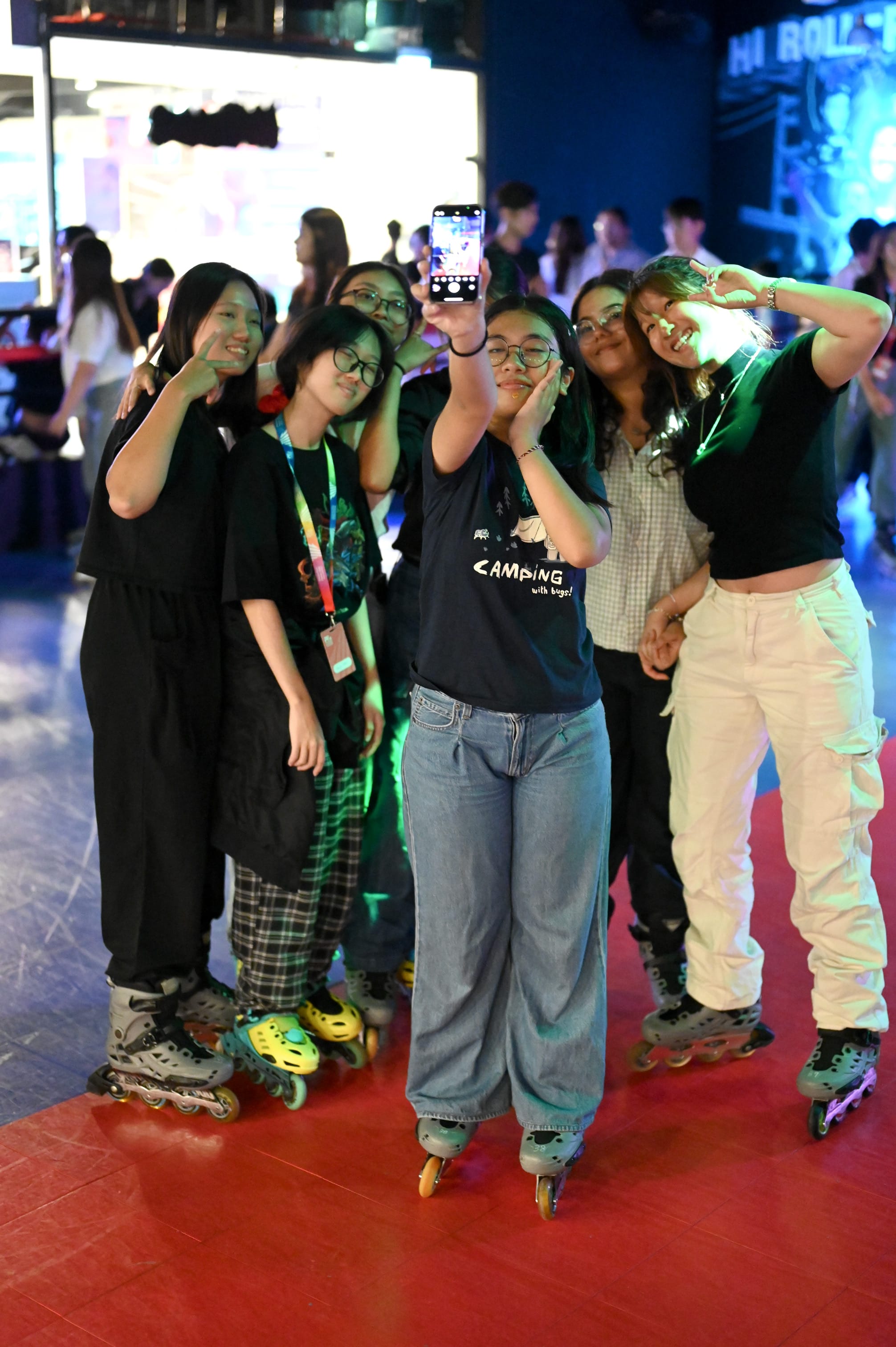 Five young women wearing inline skates pose together for a selfie at an indoor roller skating rink.
