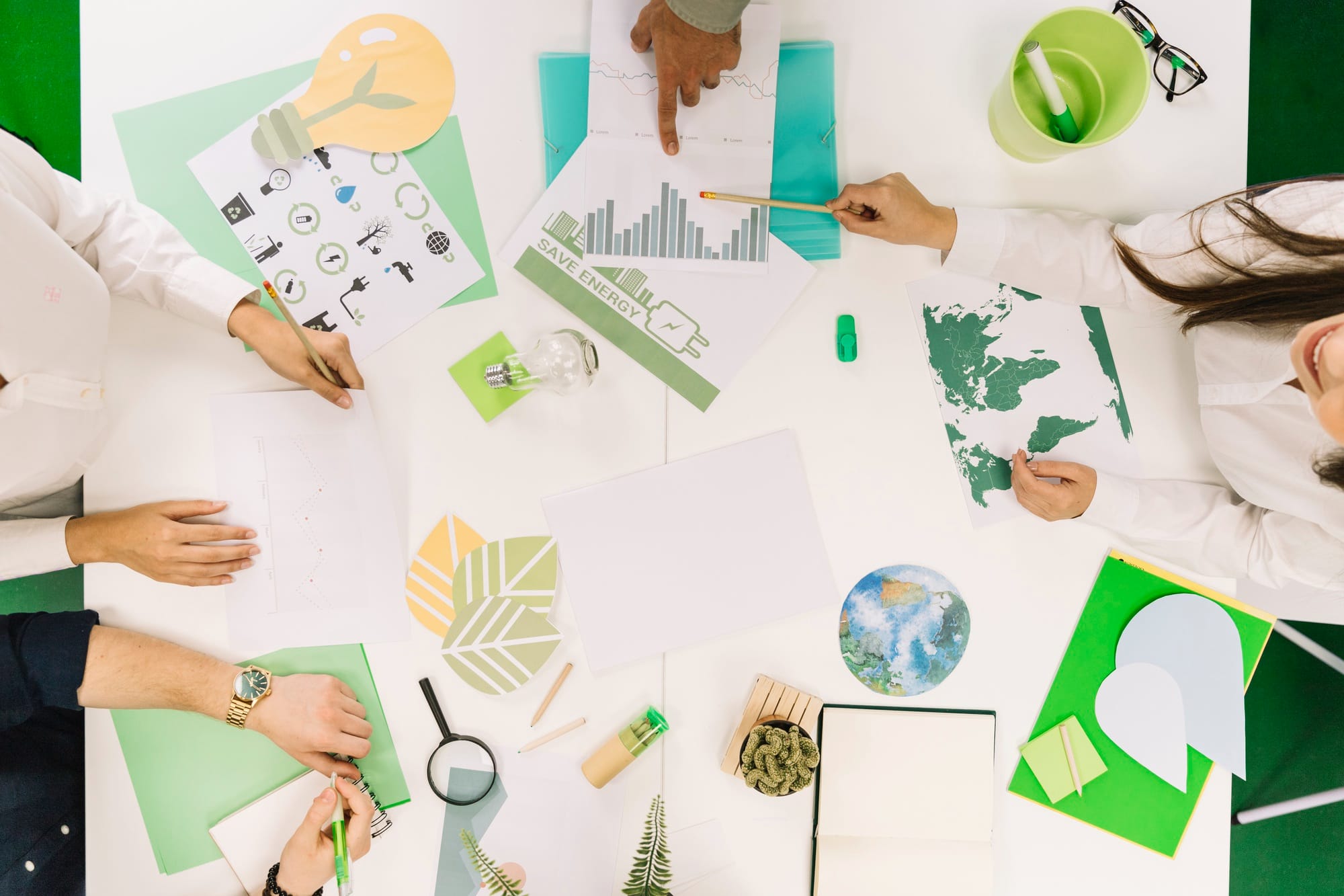 Overhead view of people collaborating at a table covered with green-themed sustainability charts, maps, and eco icons.