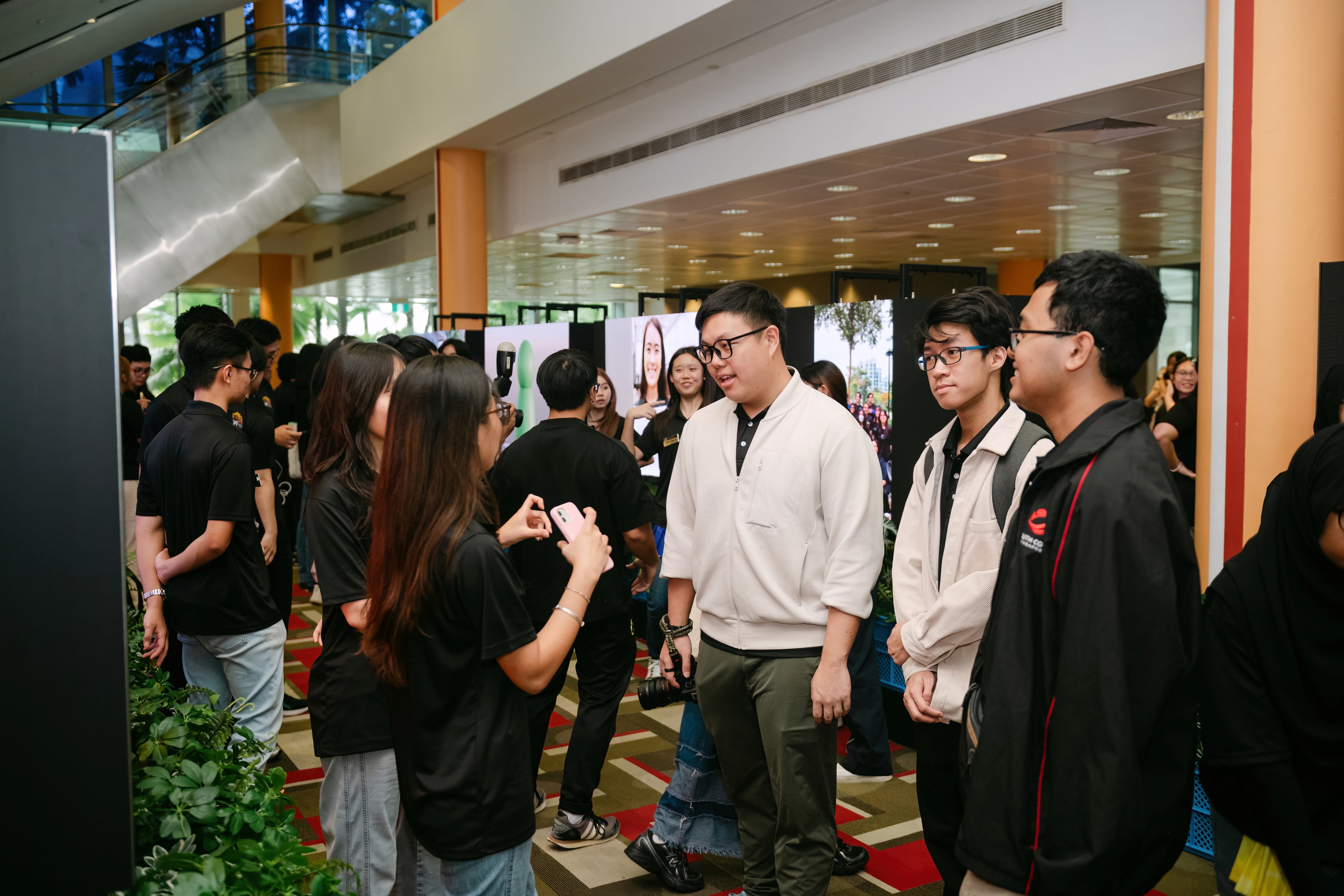 A group of young people talking in an indoor exhibition hall with portrait photos displayed on panels behind them.