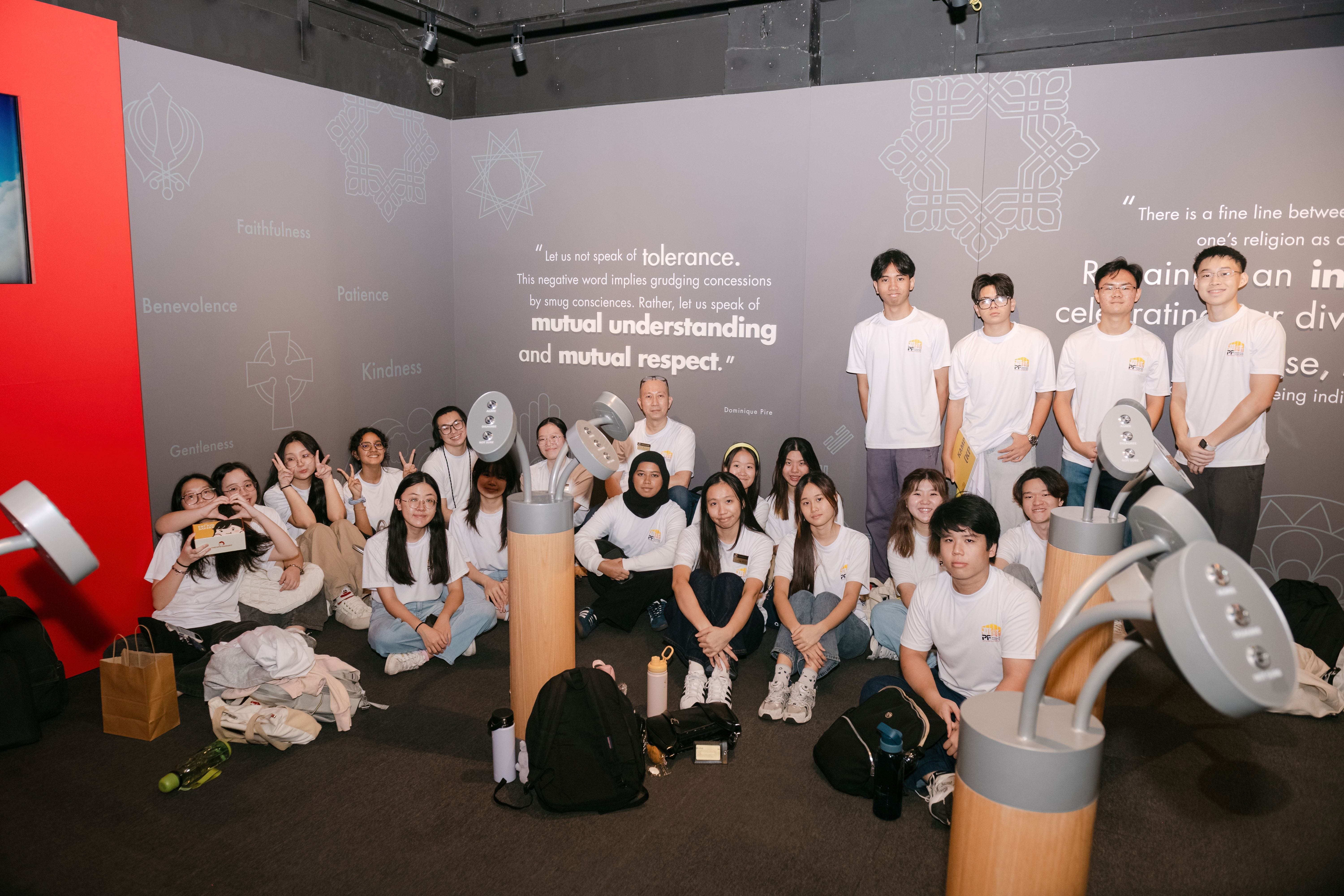 A large group of young people in white t-shirts pose together inside a museum exhibit about mutual respect and tolerance.