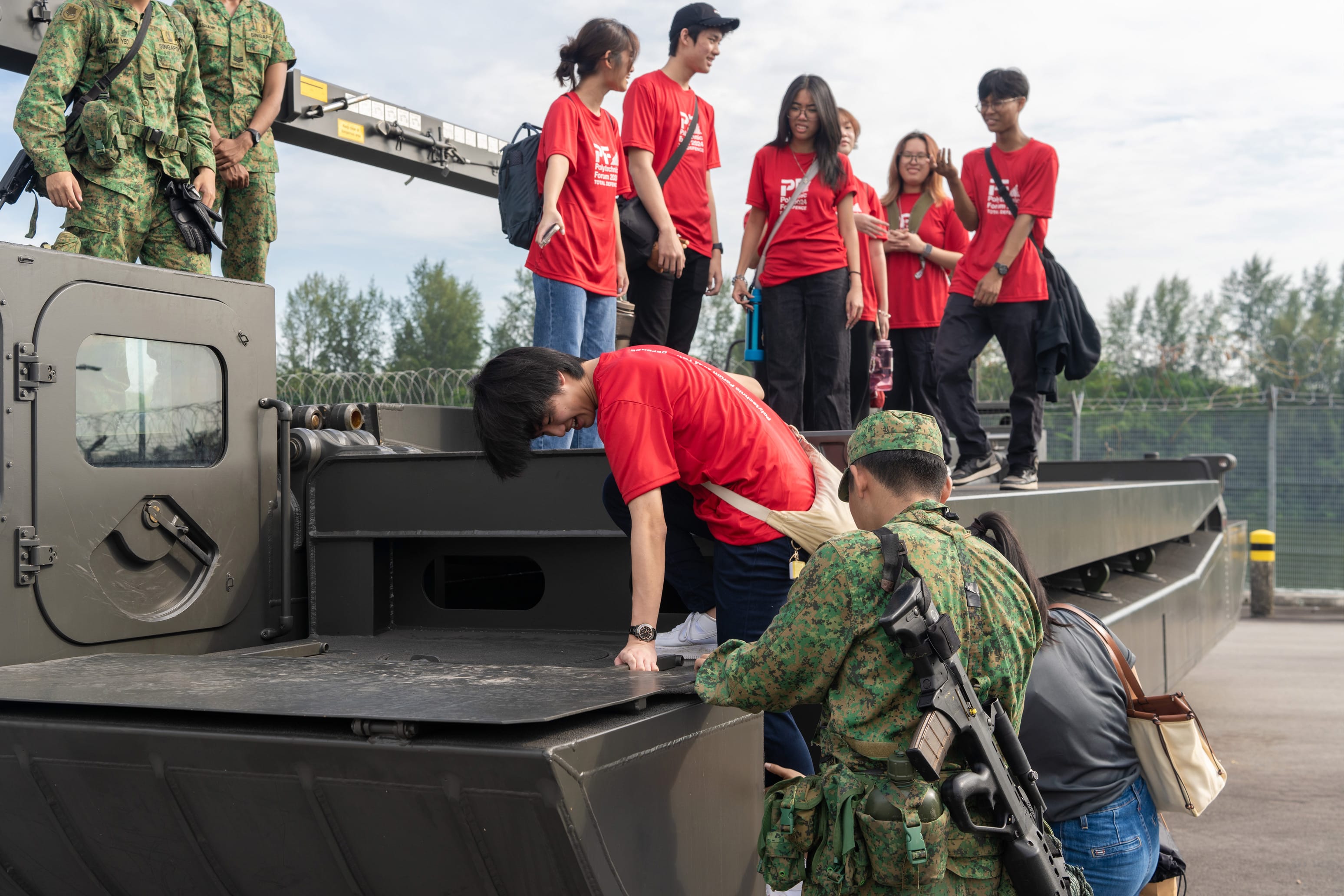Civilians in red shirts stand on a military armored vehicle while armed soldiers in camouflage assist them.