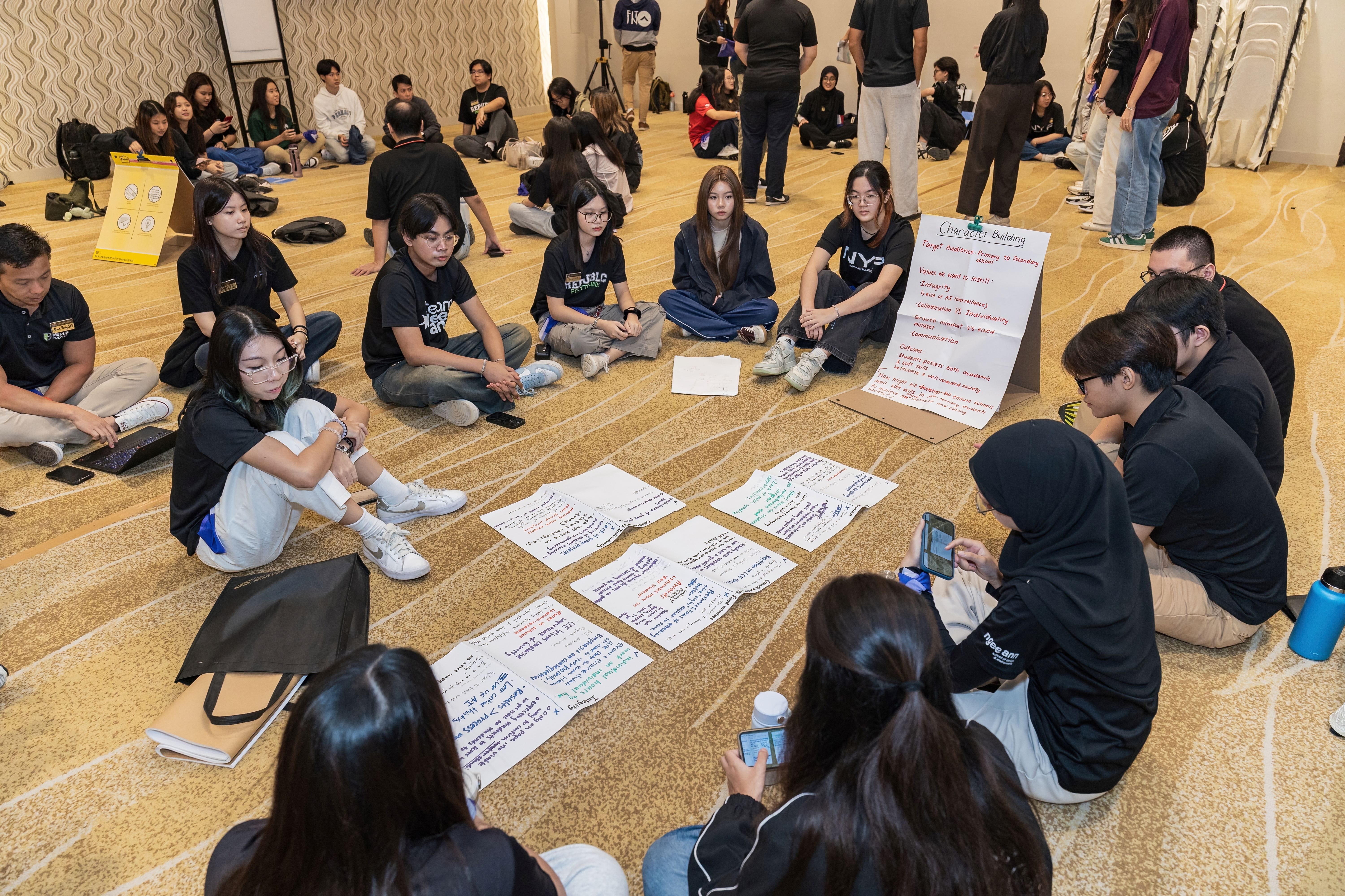 Students sit in a circle on a carpeted floor around written papers, with a Character Building poster nearby.