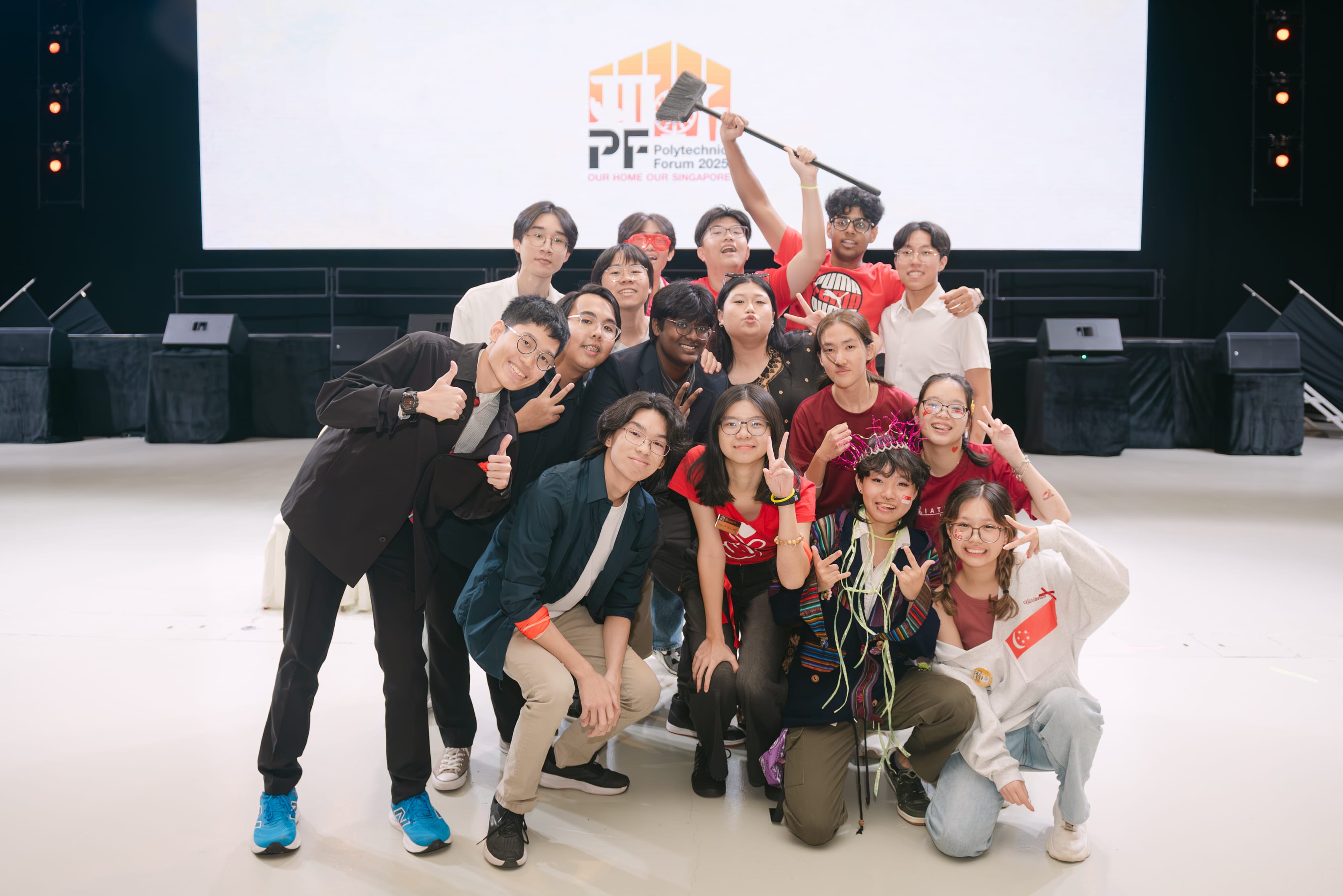 A group of smiling young people pose together in front of a Polytechnic Forum 2025 screen on a stage.