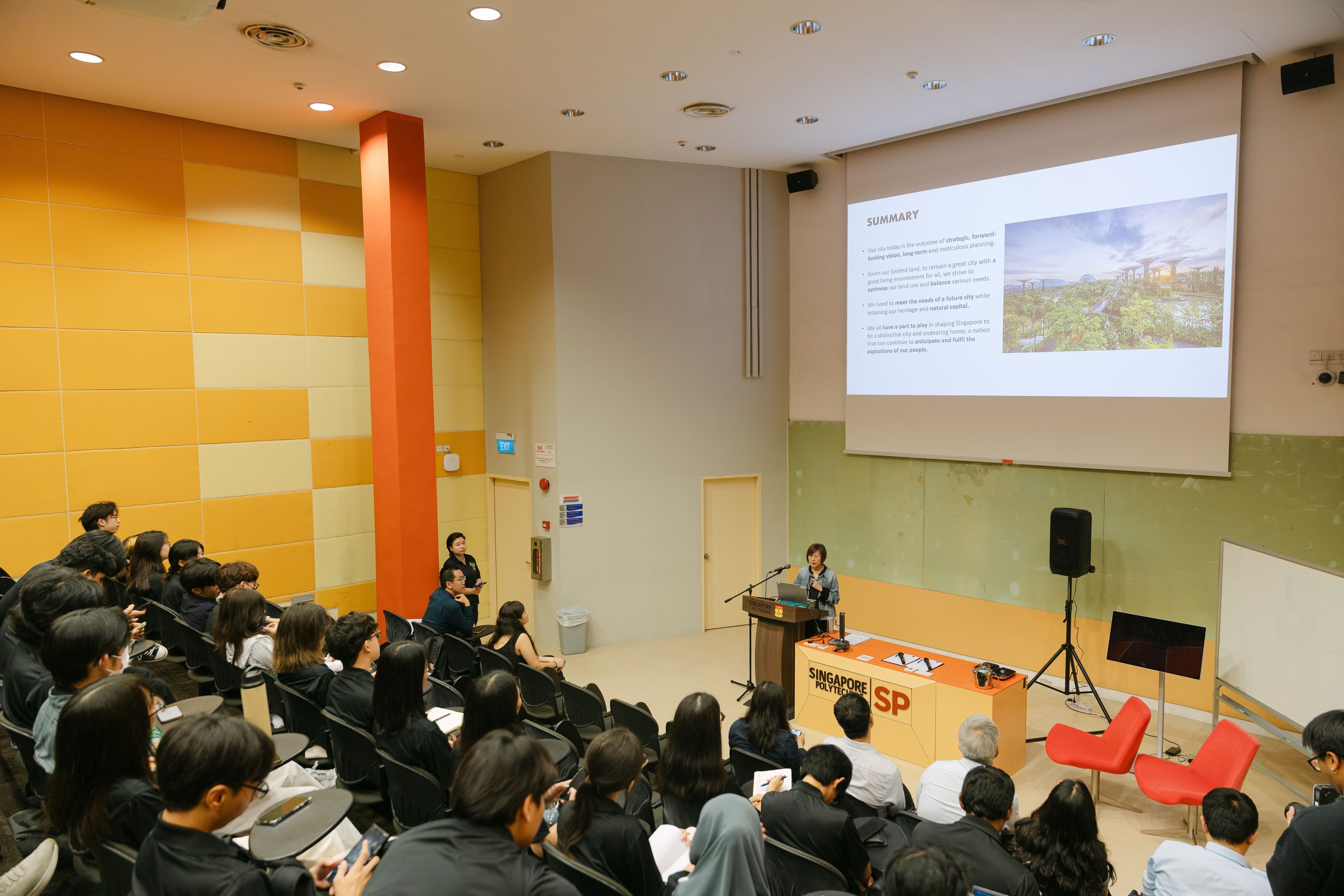 A speaker presents at a Singapore Polytechnic lecture hall with a Summary slide projected on screen before a seated audience.