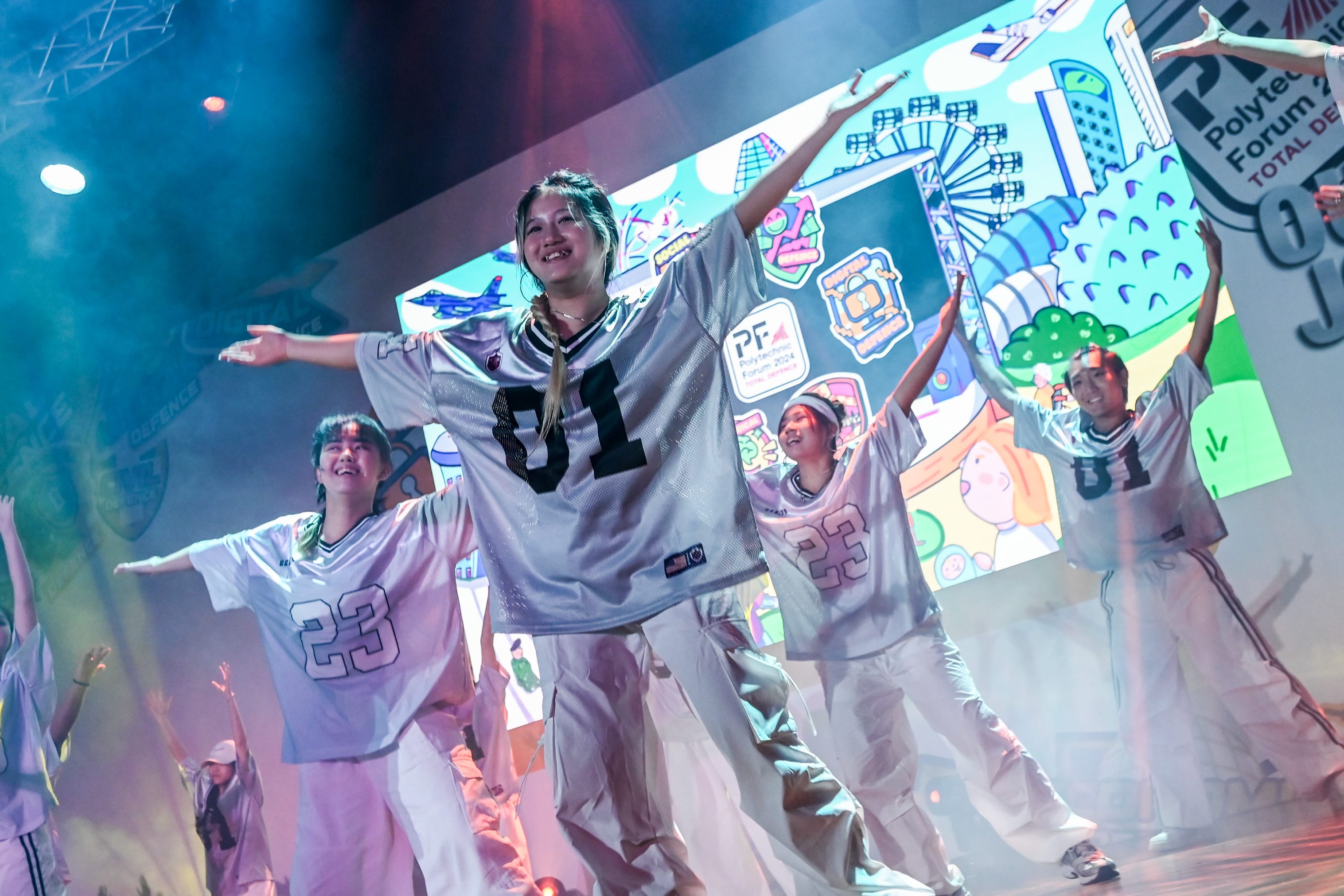 Young dancers in numbered sports jerseys perform on a colorful lit stage at Polytechnic Forum 2024.