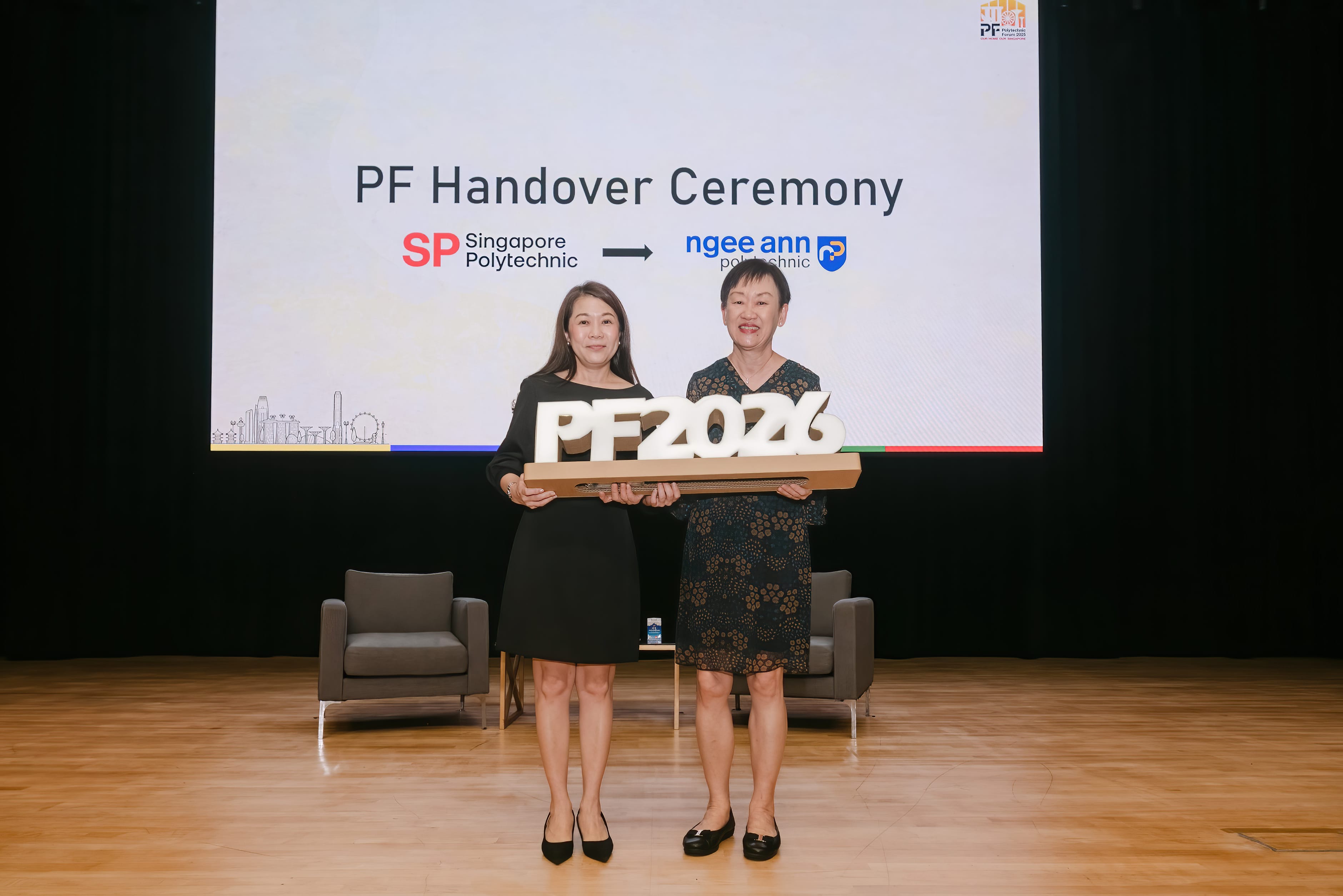 Two women on a stage hold a PF2026 sign at a PF Handover Ceremony from Singapore Polytechnic to Ngee Ann Polytechnic.